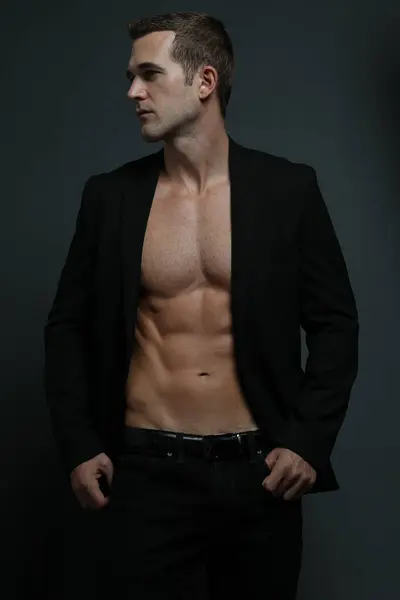 Gömleksiz, karın kaslarını ve yan bakan göğüs kaslarını göstermek için paltosu açık.