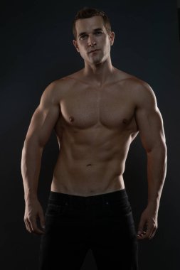 Gömleksiz fitness adamı ellerini kenetliyor ve kaslarını gösteriyor.