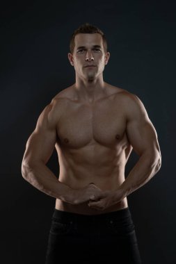 Gömleksiz fitness adamı ellerini kenetliyor ve kaslarını gösteriyor.