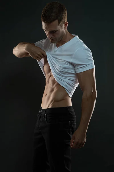 Kaslı Adam karın kaslarını göstermek ve aşağı bakmak için gömleğini çıkararak soyunuyor.