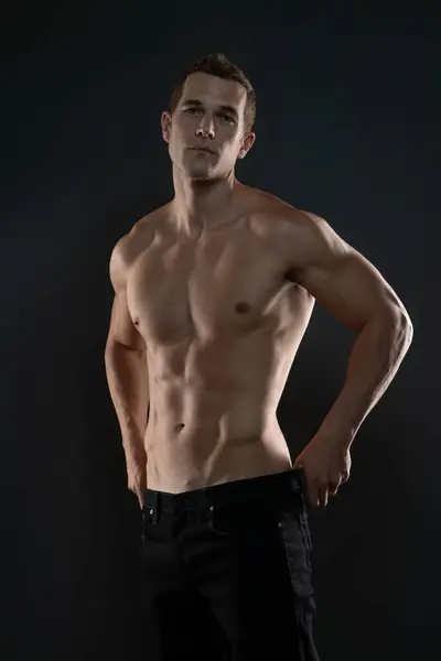 Elleri kalçasında, kaslı vücudunu gösteren üstsüz bir adam. 