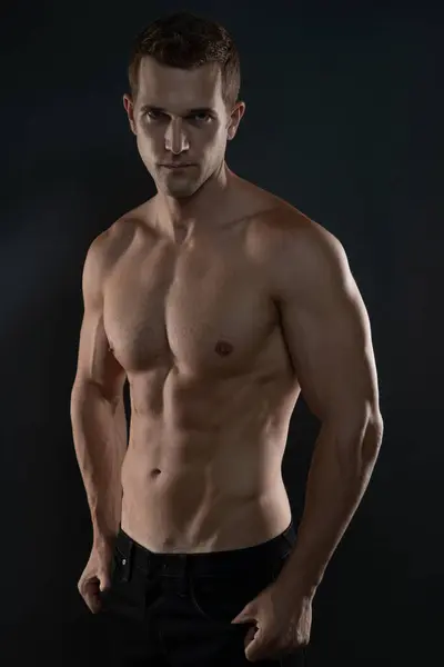 Erkek model kameraya ciddi bakıyor ve kaslarını gösteriyor.