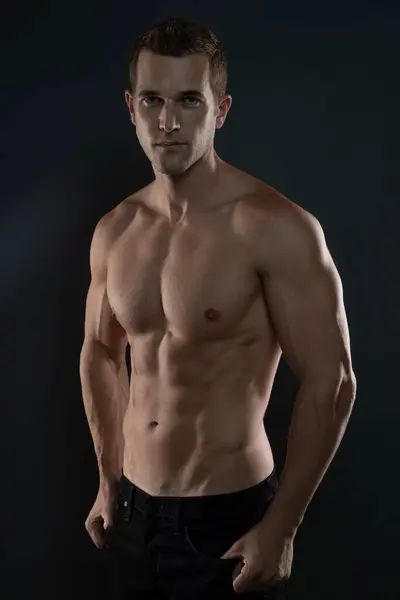 Gömleksiz adam ileriye bakan kaslarını gösteriyor.