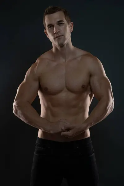 Gömleksiz fitness adamı ellerini kenetliyor ve kaslarını gösteriyor.