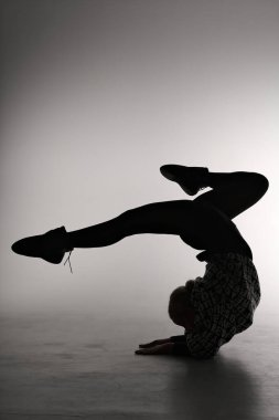 Gri arka planda poz veren genç bir balerin. Balerin siyah elbise ve dans ayakkabısı giyiyor. Çizgi çekimi - kız silueti.