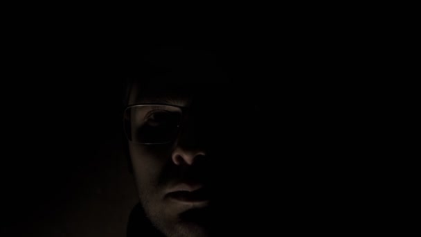 戴眼镜的男人在黑色背景上对着镜头看低调的愤怒和变态的情绪 恐怖的狂热者面对着脉动的光 精神紊乱 — 图库视频影像