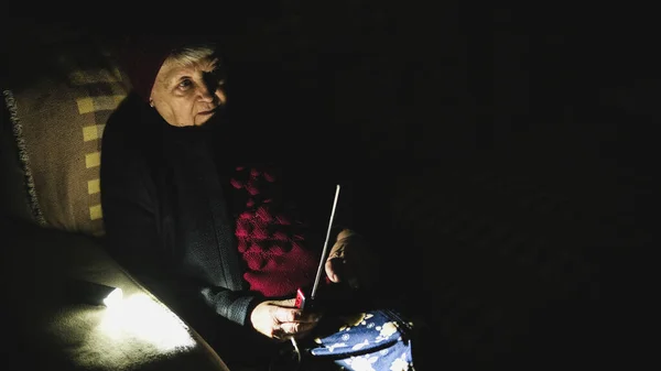 Ukrayna: Büyükannem, Rusya 'nın terör saldırıları sırasında karanlıkta elinde telsizle oturuyordu. Kış kıyafetleri içinde kıdemli bir kadın. Kanepede, el radyo alıcısı ile haberleri dinliyor..