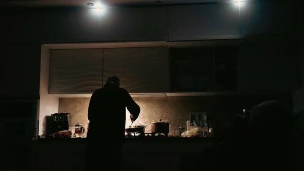 Man cooking with flashlights on a kitchen during blackout in ukraine. Blackout in Ukraine concept. Man cooking in a darkness with flashlights around.