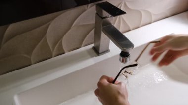 close up of a person washing the eyes glasses underflow water in the white sink with soap. Glasses care concept, hygiene for eyes.