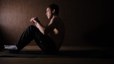 Healthy Man with naked torse Exercising Abdominals On mate at home with side lightning in dark room at home.