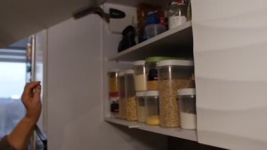 Old senior woman hands takes something from top shelf of a kitchen cabinet at home, opens the doors, cooking, domestic chores at maternity leave.