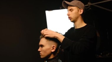 Barber shop. Man in barber's chair, hairdresser styling his hair with hands in dark key lightning. Hairdresser for man. Slow motion.