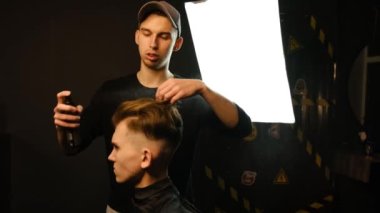 Barber makes hair styling with hair spray after haircut at the barber shop. Young handsome Caucasian man getting a haircut in a modern hairsalon from professional hairdresser. Slow motion