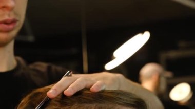 Close up Barber master hairdresser does hairstyle and style with scissors and comb. Concept Barbershop. side view in dark key lightning with warm light. Slow motion