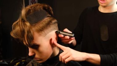 men's hairstyling and haircutting with barber shaving machine, hair cut for male. Hairdresser service with shaver in a modern barbershop in a dark key lightning with warm light side view. Slow motion