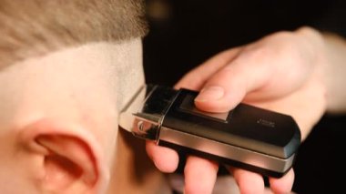 close up men's hairstyling and haircutting with barber shaving machine, hair cut for male. Hairdresser service with shaver in a modern barbershop in a dark key lightning Slow motion.