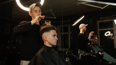 Barber master hairdresser does hairstyle and style with scissors and comb. Concept Barbershop. side view in dark key lightning with warm light.