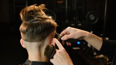 Yakışıklı bir berberin, saç kesme makinesi kullanarak müşterisine saçını keserken görüntüsü. Modern bir berber dükkanındaki kuaför servisi. Ilık ışıklı arka görüşlü karanlık bir anahtar yıldırımında..