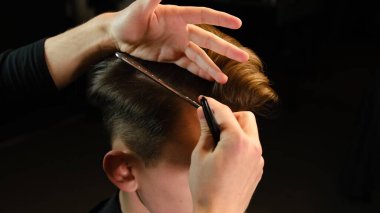 Closeup View Of barber using hair clip and comb to fix hair for cut and styling it Hairdresser use pinsn hair salon. service in a modern barbershop in a dark key lightning with warm light back view.