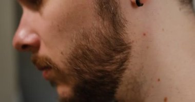 Ciddi bir genç adam tıraş makinesiyle banyoda sakalını kesiyor..