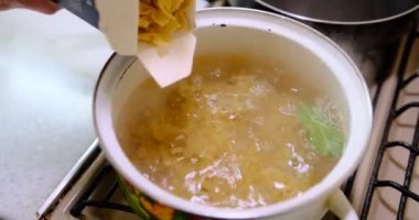 Kadın evde ocakta pişirilen haşlanmış suya makarna ekliyor..