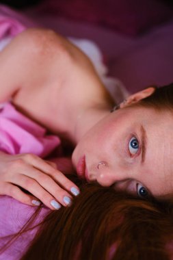 Çekici, genç, kızıl saçlı, kızıl saçlı, çarşafların üzerinde vahşi bir kadın. Yüzü yastığın altında, taze, pembe çarşaflı yatak odasında yatıyor.