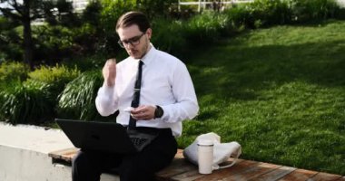 Uzaktan çalışan erkek serbest çalışan kulaklıklar ve laptop video konferansı ya da şehir parkında bir bankta bir erkekle buluşma mesafeleri modern bir kentsel arka plan, dışarıda, dışarıda.