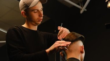 Barber master hairdresser does hairstyle and style with scissors and comb. Concept Barbershop. back view in dark key lightning with warm light.