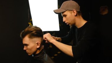 Barber master hairdresser does hairstyle and style with scissors and comb. Concept Barbershop. side view in dark key lightning with warm light.