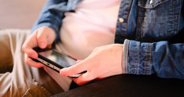 Beyaz tişörtlü ve kot pantolonlu bir adamın kahverengi bir kanepede oturan el bilgisayarı konsoluyla oynadığı bir oyuna dalın. Yaşam tarzı ve oyun temalı videolar için ideal seçici odak.