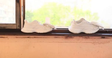 Sneakers yeşil arka planda pencere pervazında kuruyor. Kentsel yaşam tarzı görselleri. Beyaz ayakkabılar içeride kuruyor ve dışarısı doğal.