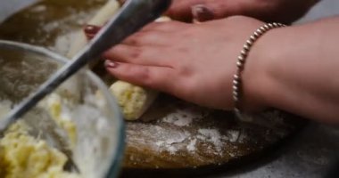 Tembel hamur köfteleri pişirmek için hamuru şekillendirip süzme peynirleri pişiren bir kadın masanın arka planında bulanık bir şekilde oturur. Ev yapımı hamur tatlısı hazırlama süreci