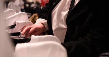 Genç bir kadın giyim mağazasındaki askılarda asılı tişörtlere göz atıyor. Bu modaya uygun kıyafet eklentileri için uygun olan çeşitli tarzları gösteren her ürünü inceliyor.