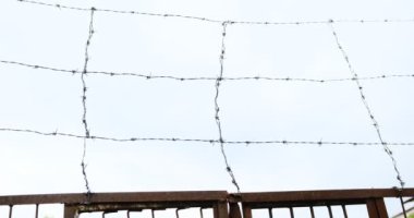 Zamanla paslanmış yıpranmış dikenli tel tel örgü, parlak mavi bulutsuz gökyüzü kavramına karşı çerçevenin her tarafına uzanır..