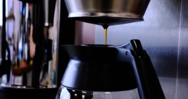 Taze demlenmiş kahve filtreleri profesyonel kahve makinesinin parlak sürahisine dönüşür. Zengin aroma ve mükemmel fincanın özünü yakalama sanatının pürüzsüz dokusunu sergiler..