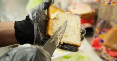 Şef, kızarmış ekmeğin üzerine kremalı peynir sosu sürer. Siyah lastik eldivenler, profesyonel bir mutfakta sandviç hazırlar. Yemek hazırlar, mutfak temizliği sandviçi yapar..