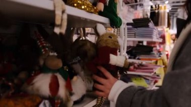 Bir kadın süslemelerle dolu bir raftan bir Noel sincabı süsü alır ve sıcak mevsimlik bir ortamda mükemmel bir bayram hediyesi seçerken dikkatlice inceler.