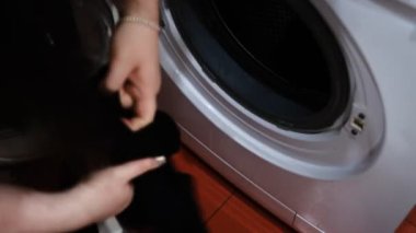 Çamaşır makinesinden çamaşırları boşaltan genç bir kadın. Parlak ve rahat bir evde günlük ev işlerini yapıyor. Temiz ve düzenli bir yaşam alanı sağlıyor..