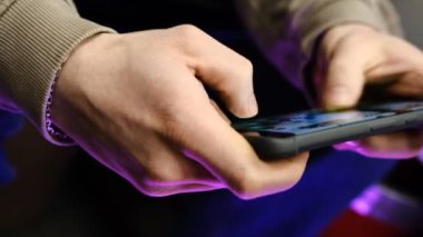 Hızlı parmak hareketleri ve renkli titreşimli el ışıkları ile mobil oyun oynayan genç adam, dinamik oyun, telefon ekranını kapat, dijital eğlence, oyun eylemi, enerjik oyun oturumu
