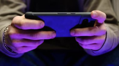 Hızlı parmak hareketleri ve renkli titreşimli el ışıkları ile mobil oyun oynayan genç adam, dinamik oyun, telefon ekranını kapat, dijital eğlence, oyun eylemi, enerjik oyun oturumu