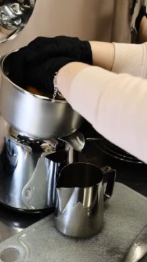 Siyah tek kullanımlık eldivenli bir barista profesyonel meyve sıkacağı üzerine taze portakal sıkıp modern bir mutfakta metal bir sürahiye doldurur ve C vitamini ile ferahlatıcı bir narenciye içeceği hazırlar..