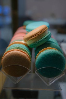 Close-up of colorful macarons with white cream filling displayed under soft lighting on a countertop with blurred background and selective focus highlighting their delicate texture and vibrant hues.. clipart