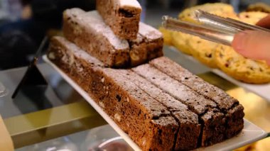 Tedarikçi, dilimlenmiş ve toz şekerle kaplanmış çikolataya düşkün tatlı tatlara düşkün zarif sunum detaylarını ele almak için metal maşa kullanıyor..