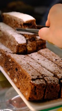 Tedarikçi, dilimlenmiş ve toz şekerle kaplanmış çikolataya düşkün tatlı tatlara düşkün zarif sunum detaylarını ele almak için metal maşa kullanıyor..