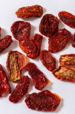 Beyaz zemin üzerine dizilmiş güneşte kurutulmuş domatesler canlı kırmızı renklerini ve doğal dokusunu vurguluyor. Akdeniz mutfağı ve gurme yemek kavramları için mükemmel.