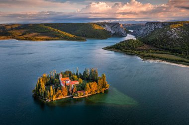 Visovac, Hırvatistan - Krka Ulusal Parkı 'ndaki Visovac Hıristiyan manastırı adasının güneşli bir sonbahar sabahı, dramatik bir altın gün doğumu, sonbahar yeşilliği ve berrak turkuaz mavi su manzarası