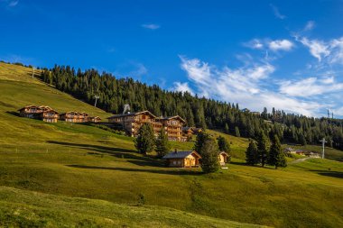 Seiser Alm, İtalya - Alpe di Siusi 'de güneşli bir yaz gününde mavi gökyüzü ve bulutlarla dolu tipik ahşap oteller ve kiraz ağaçları ve yeşil alanlar