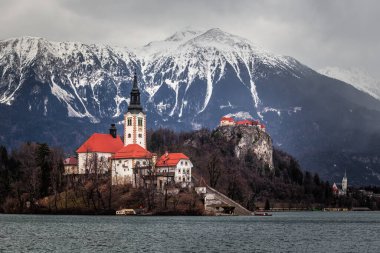 Bled, Slovenia - Beautiful view of Lake Bled (Blejsko Jezero) with Pilgrimage Church of the Assumption of Maria on Bled Island, Bled Castle and snowy Julian Alps at background at winter time with cloudy sky