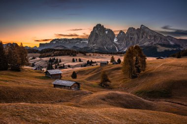 Alpe di Siusi, İtalya - Seiser Alm, Saslonch (Sassolungo veya Langkofel) dağıyla birlikte ılık bir sonbahar gündoğumu olan Alpe di Siusi, İtalya Dolomitler ve ahşap kulübeler ve renkli gökyüzü ve bulutlar