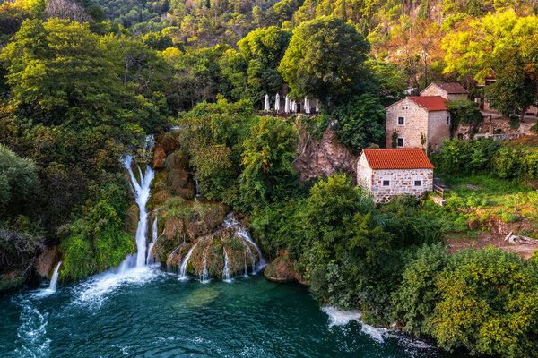 Krka, Croatia - Aerial view of the beautiful Krka Waterfalls in Krka National Park on a bright summer morning with traditional small houses and green foliage and turquoise water